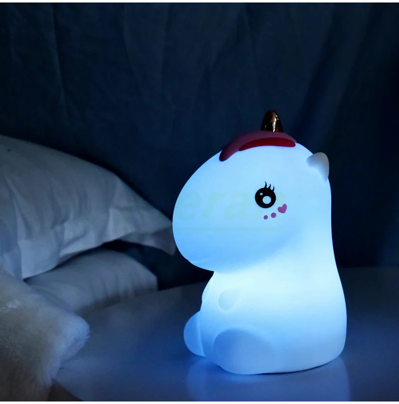 A white unicorn LED night light with a pink horn and touch control resting on a dark surface.