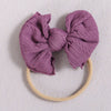 A purple knitted bow headband with a light beige elastic band.