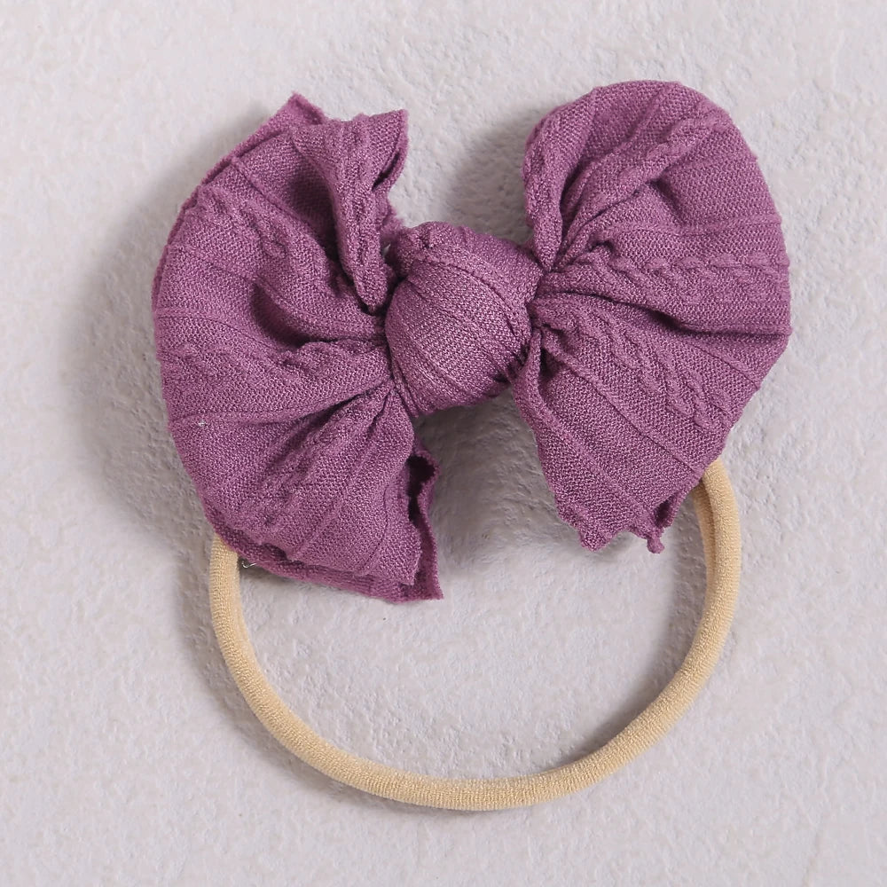 A purple knitted bow headband with a light beige elastic band.