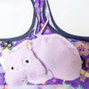A soft purple pygmy hippo plush toy is shown lying on a purple fabric background.