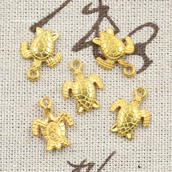 A collection of small, gold-colored sea turtle charms for jewelry making displayed on a light fabric background.