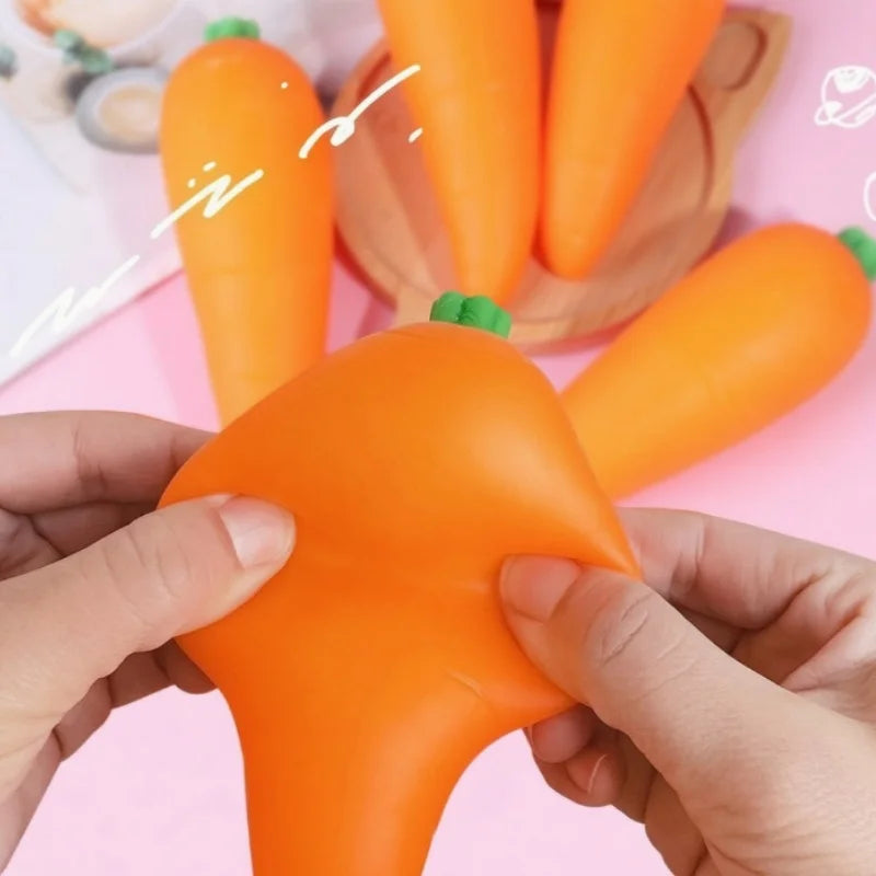 A hand is squeezing an orange carrot squishy stress relief toy against a pink background.
