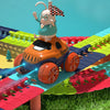 A rabbit character wearing glasses and a checkered flag sits on an orange race car track set with green and red terrain.