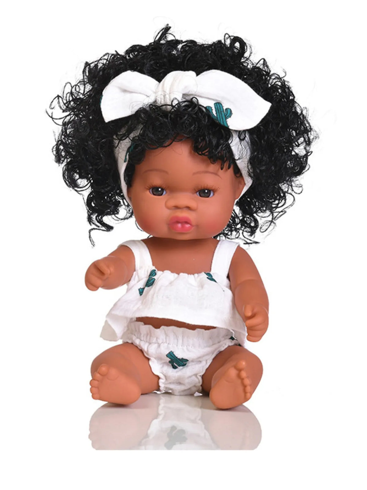 A dark-skinned baby doll with curly hair wearing a white outfit and a white bow
