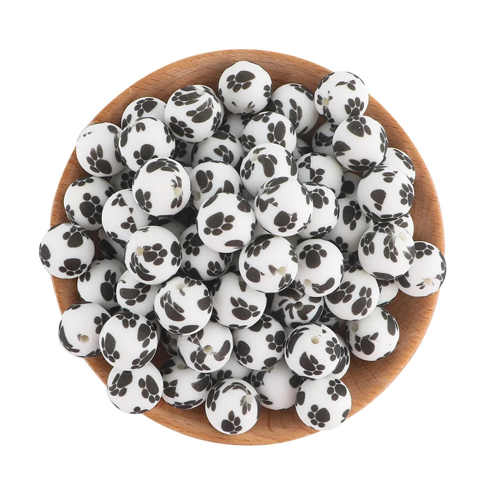 A pile of small, round, black and white silicone beads for jewelry making in a wooden bowl.