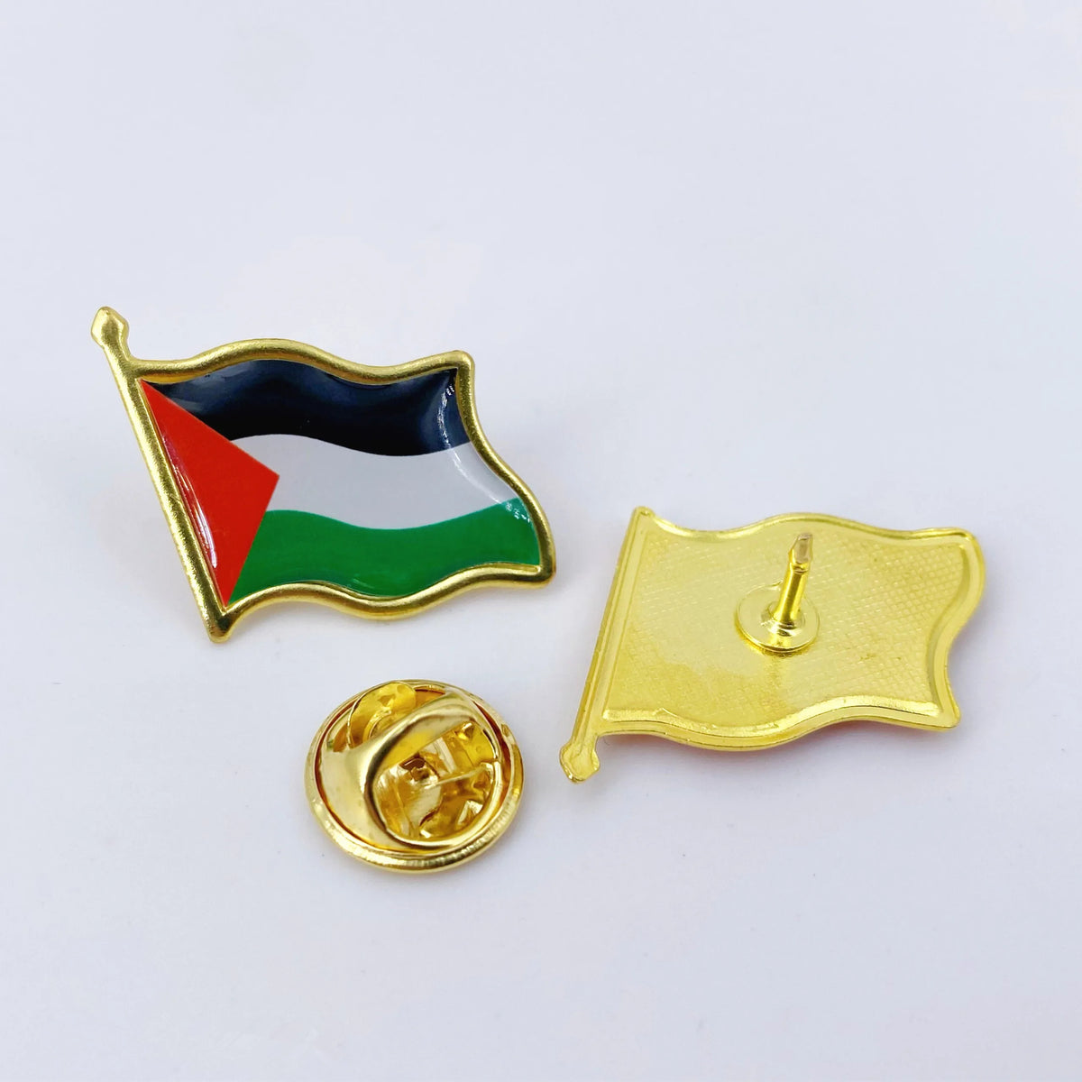A lapel pin featuring the flag of Palestine with a green, white, and black design on a gold-colored metal background.