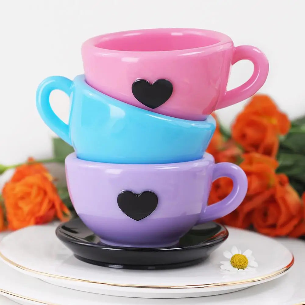 Une pile de trois tasses en silicone en forme de cœur rose, bleu et violet sur une assiette blanche.