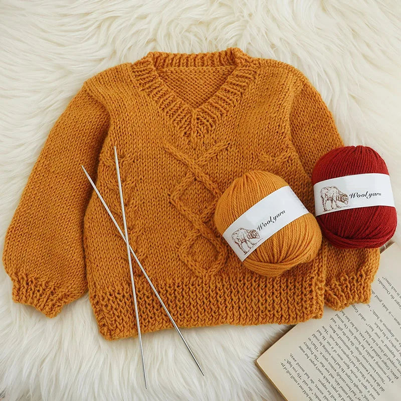 A knitted orange wool sweater lying on a white fluffy surface with a ball of red yarn nearby.