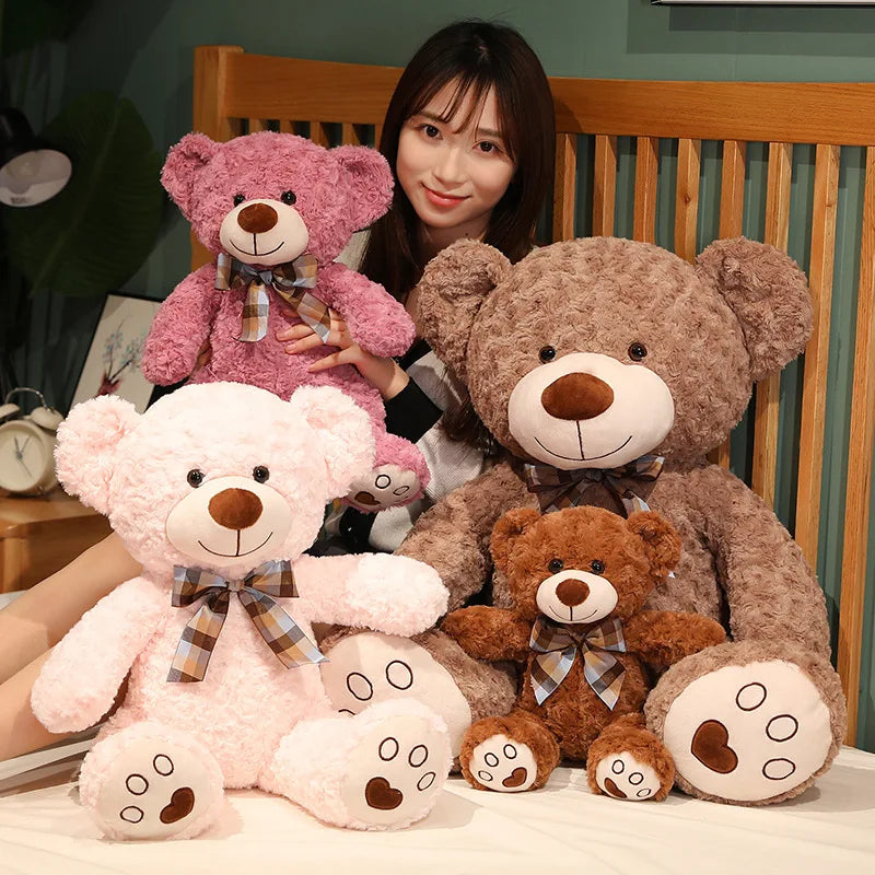 A collection of pink and brown teddy bear plush pillows with bows displayed in front of a wooden headboard.