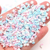 A hand holds a pile of polymer clay slices assortment in pink, blue, and white colors for DIY crafts.