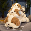 A fluffy brown and white dog plush toy lying down on a gray surface.