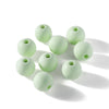 A collection of pale green matte acrylic round beads scattered on a white surface.