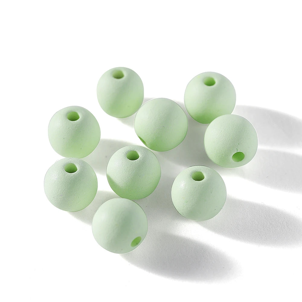 A collection of pale green matte acrylic round beads scattered on a white surface.