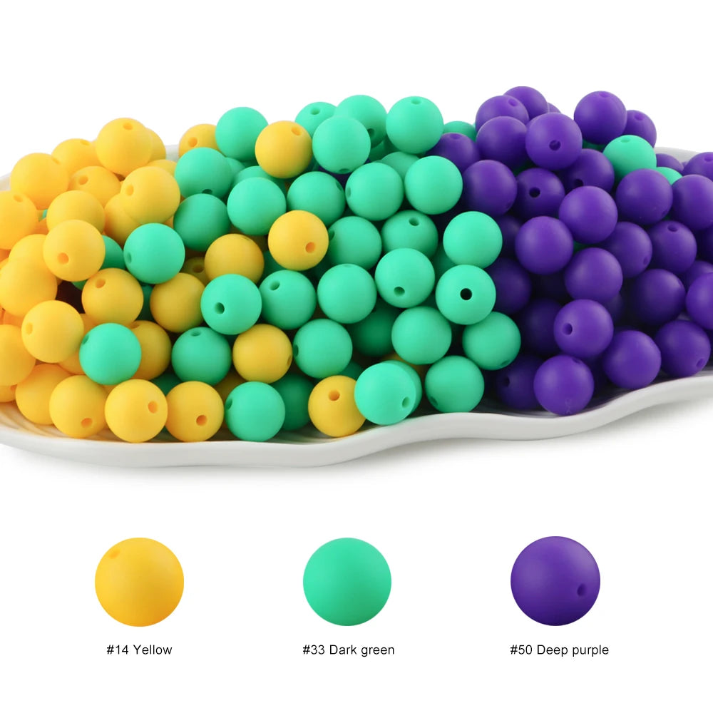 A collection of round silicone beads in yellow, green, and purple are displayed on a white plate.