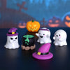 Una colección de figuras fantasma blancas, una bruja morada y un adorno de calabaza naranja sobre una superficie oscura.