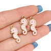 Two pink and white enamel marine life charms are displayed on a hand.