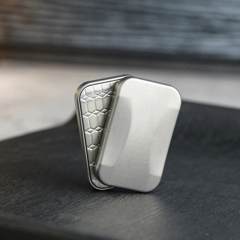 A silver metal fidget slider with a textured surface is shown resting on a dark surface.