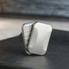 A silver metal fidget slider with a textured surface is shown resting on a dark surface.