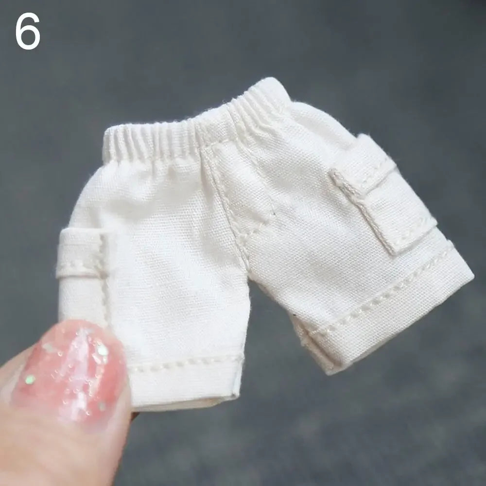 Shorts en jean blancs pour accessoires de poupée, tenus par un doigt.