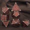 A set of seven polyhedral metal dice, including a d20 and a pyramid die, resting on dark fabric.