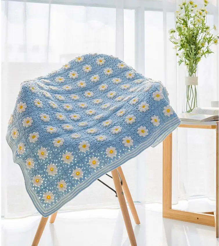 Light blue knitted blanket featuring a pattern of small yellow flowers displayed on a wooden stand.