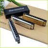 Un set de trois harmonica, incluant une housse noire et deux modèles en laiton, posés sur du papier brun.