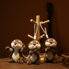Three small brown plush otters standing on a wooden surface with wooden charms in the background.