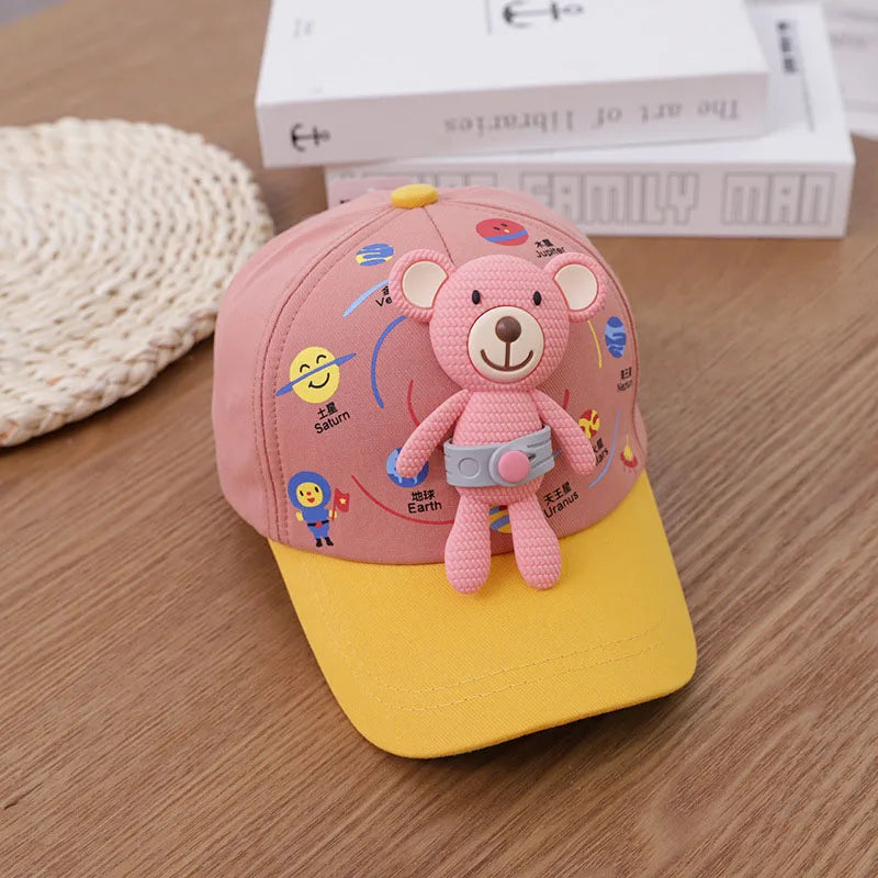 A pink toddler 3D bear baseball cap with an adjustable strap resting on a wooden surface.