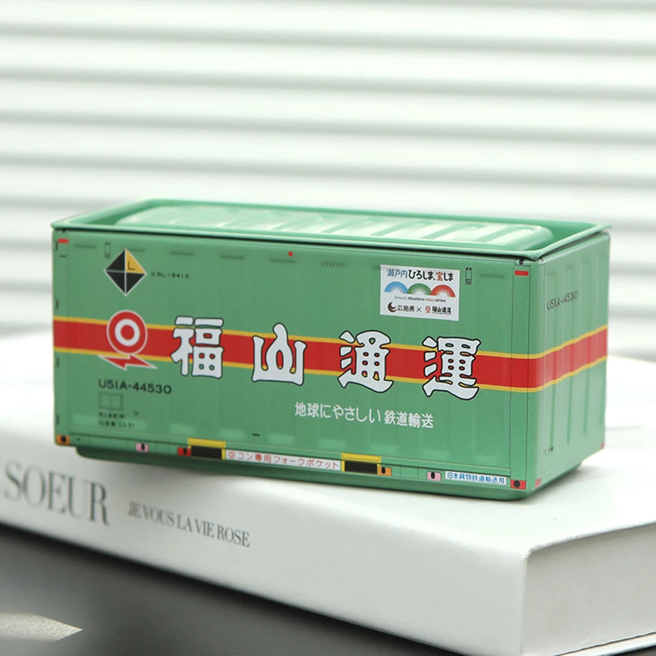 A rectangular green storage box labeled with Japanese text and a logo, resting on a white book.