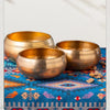 A set of three handcrafted brass Tibetan singing bowls resting on a blue patterned cloth.