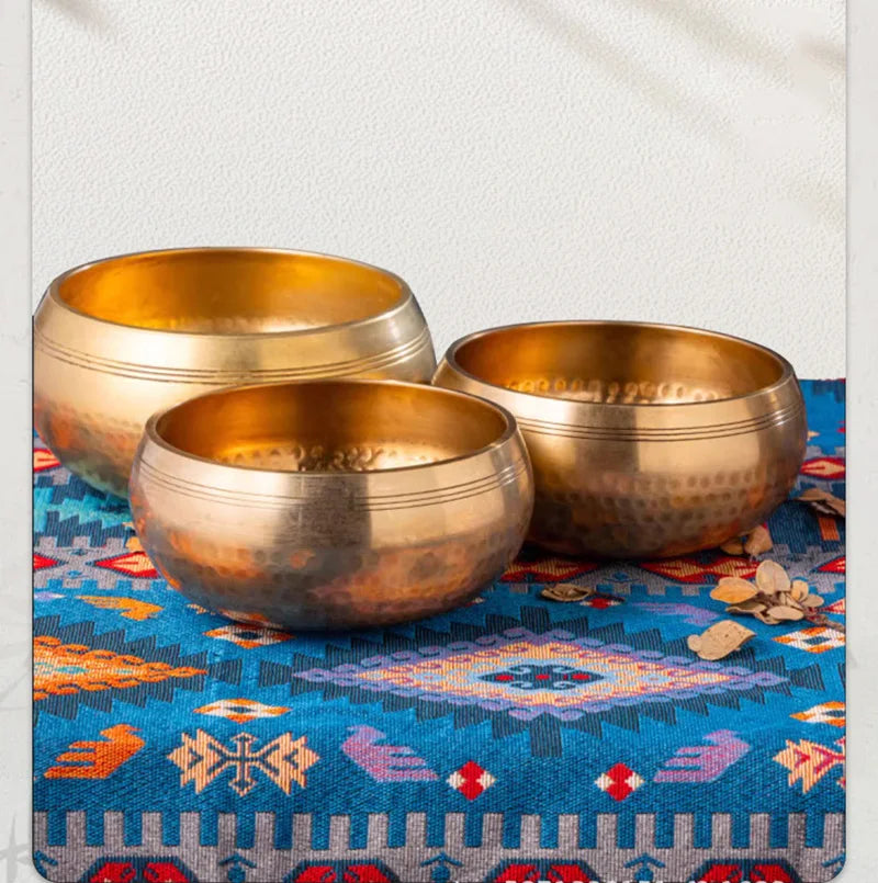 A set of three handcrafted brass Tibetan singing bowls resting on a blue patterned cloth.
