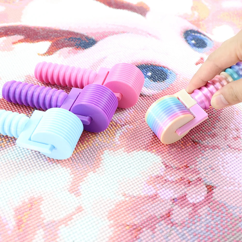 A hand holds a colorful, detachable diamond painting roller with various colored cylinders on a pink background.