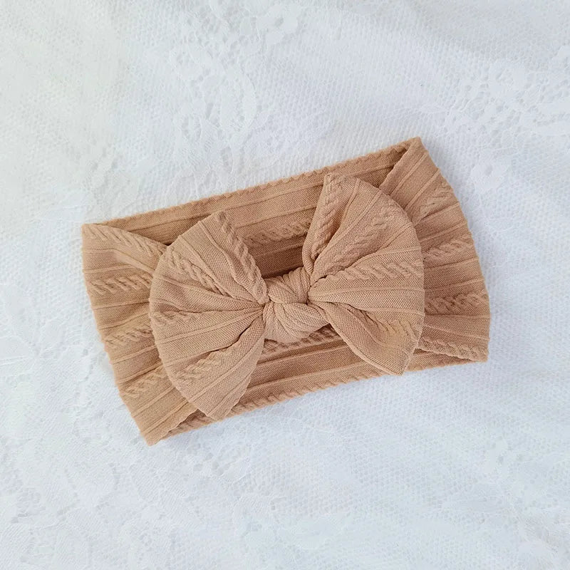A beige knitted baby headband with a large bow shown on a white background.