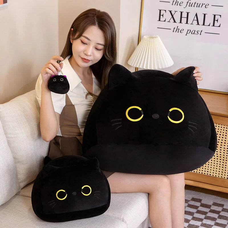 A woman is holding a large black cat plush toy and a smaller black cat plush toy on a white sofa.