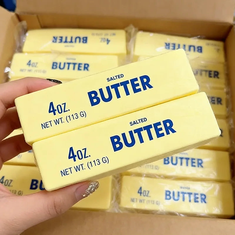 A hand holds several yellow butter squishy toys packaged in a cardboard box.