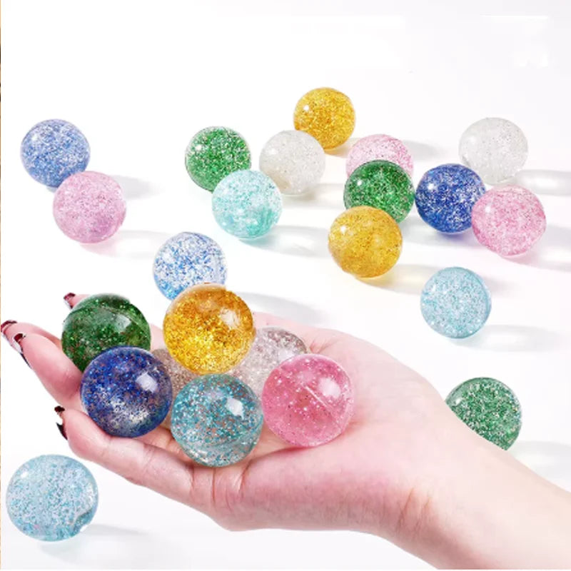 A hand holds a collection of colorful glitter bouncy balls in various shades and sizes.