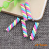 A set of ten polymer clay marshmallow charms in pink, blue, and yellow spiral colors resting on a gray textured surface.