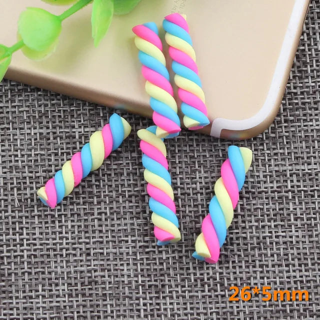 A set of ten polymer clay marshmallow charms in pink, blue, and yellow spiral colors resting on a gray textured surface.