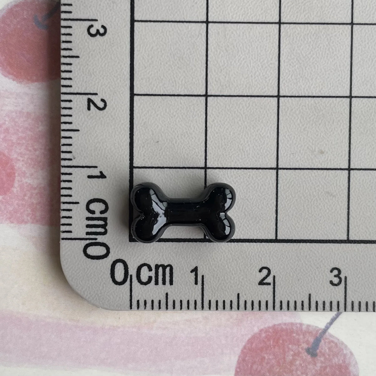 A black resin bone charm is shown next to a ruler marked in centimeters.