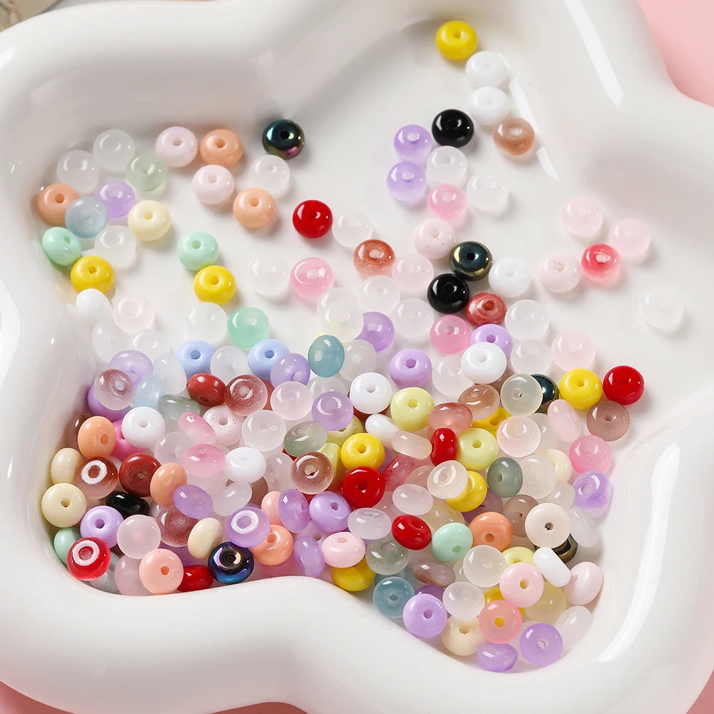 A close-up view of a white dish filled with a variety of colorful glass spacer beads in various shades of pink, purple, yello