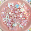 A pile of pink and iridescent acrylic bow and flower beads for DIY jewelry making in a light pink bowl.