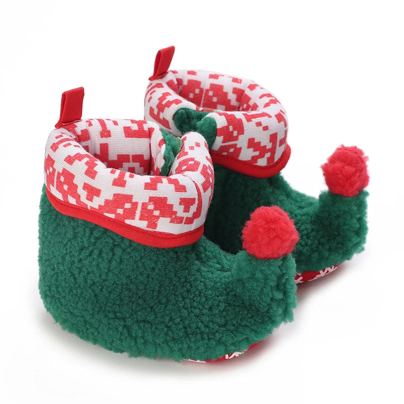 A pair of green fuzzy animal-themed baby first walker shoes with red accents and pom-poms.