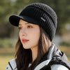 A woman wearing a black knit beanie with a brim and a white jacket outdoors.