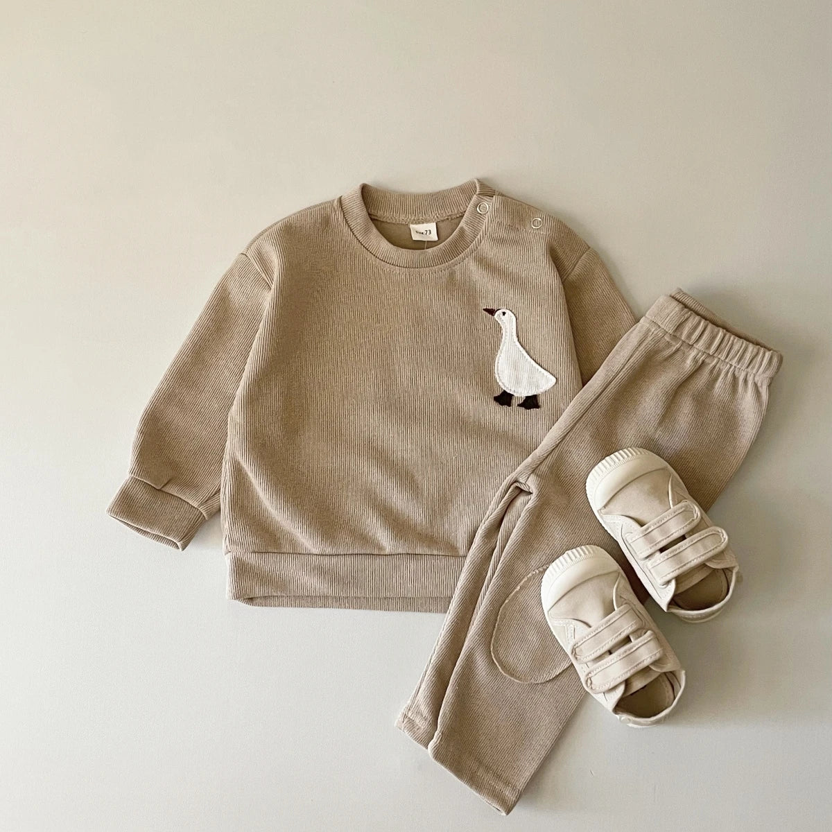 A beige baby long sleeve cartoon top and pants set featuring a white bird design.