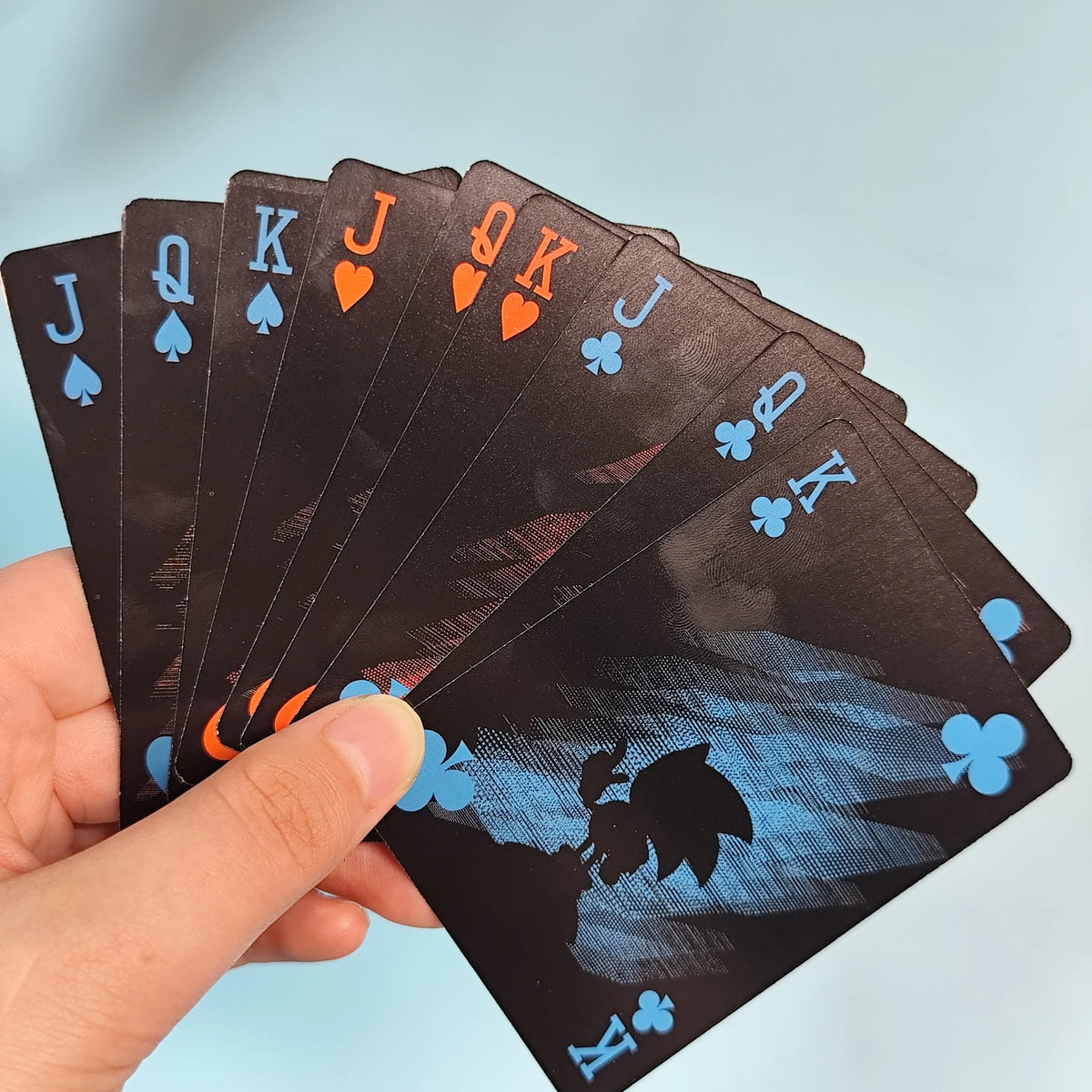 A hand holds a fan of black playing cards showing face cards like Jack, Queen, and King.