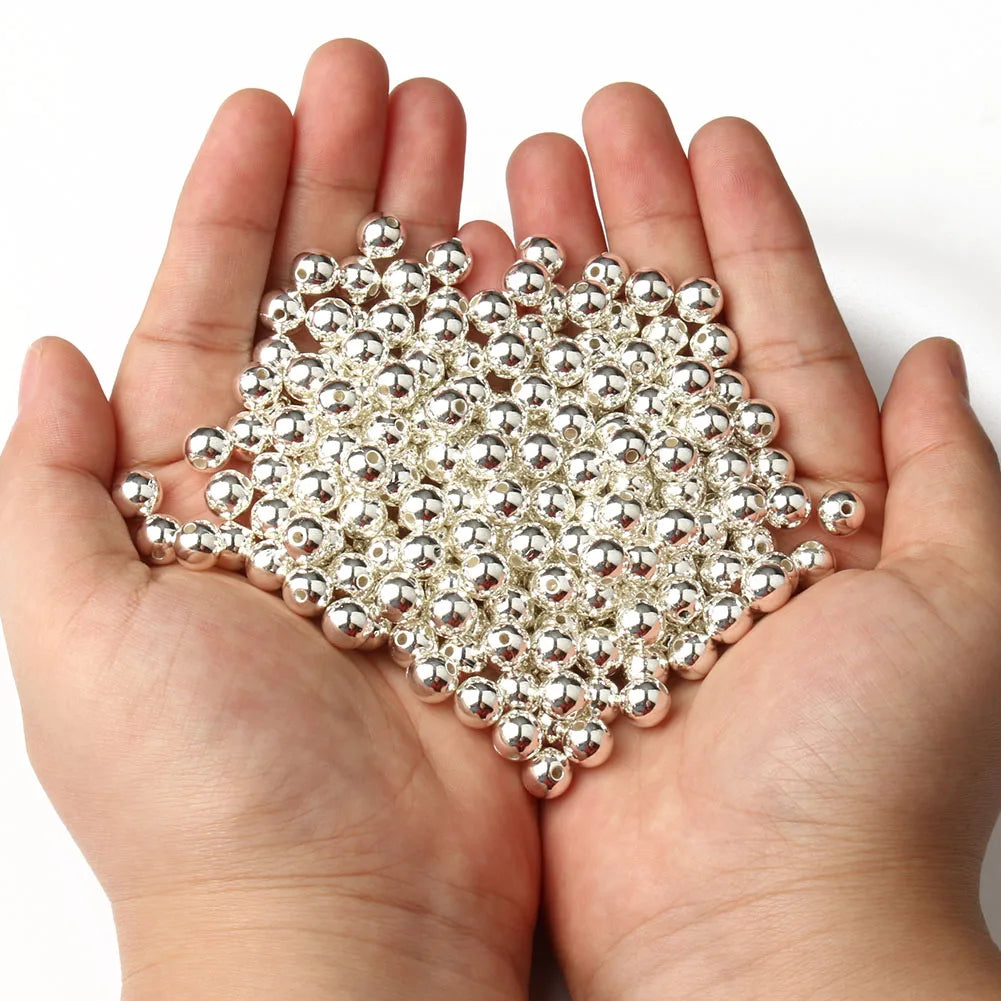 A hand holds a cluster of round silver spacer beads for DIY jewelry making