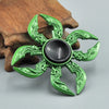 A green metal fidget spinner with intricate, leaf-like detailing rests on a wooden surface.