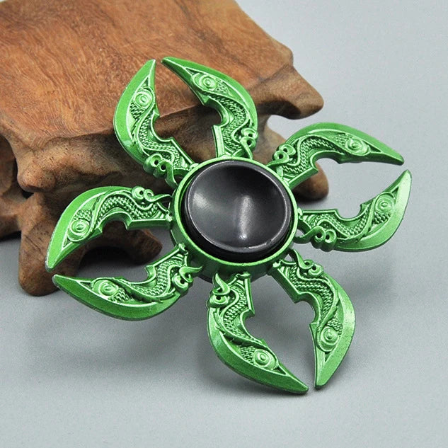 A green metal fidget spinner with intricate, leaf-like detailing rests on a wooden surface.