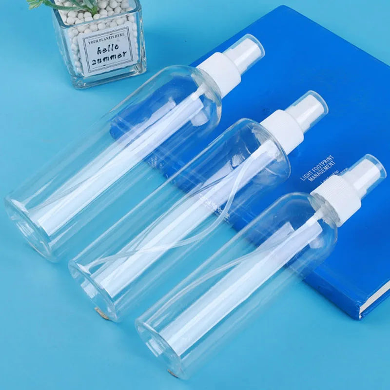 A set of three clear glass refillable travel spray bottles with white pumps resting on a blue surface.