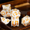 A set of seven white cheese-themed polyhedral dice resting on a dark wooden surface.